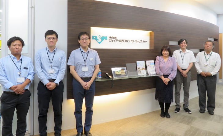 株式会社ジェイアール西日本デイリーサービスネットの受付の前に並ぶ、ご担当者 6 名の写真