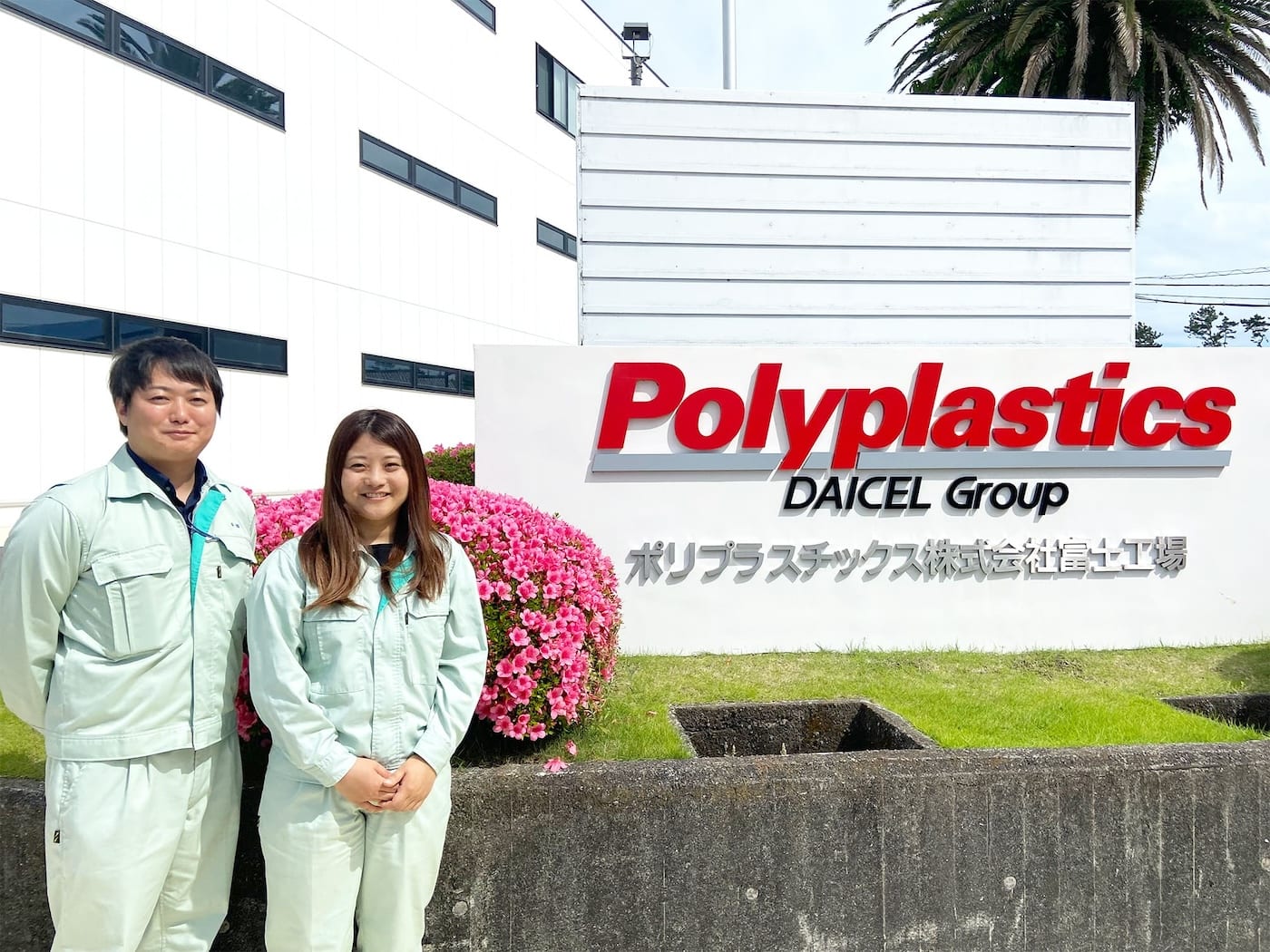 ポリプラスチックス株式会社 富士工場の看板の前に立つ、ご担当者 2 名の写真