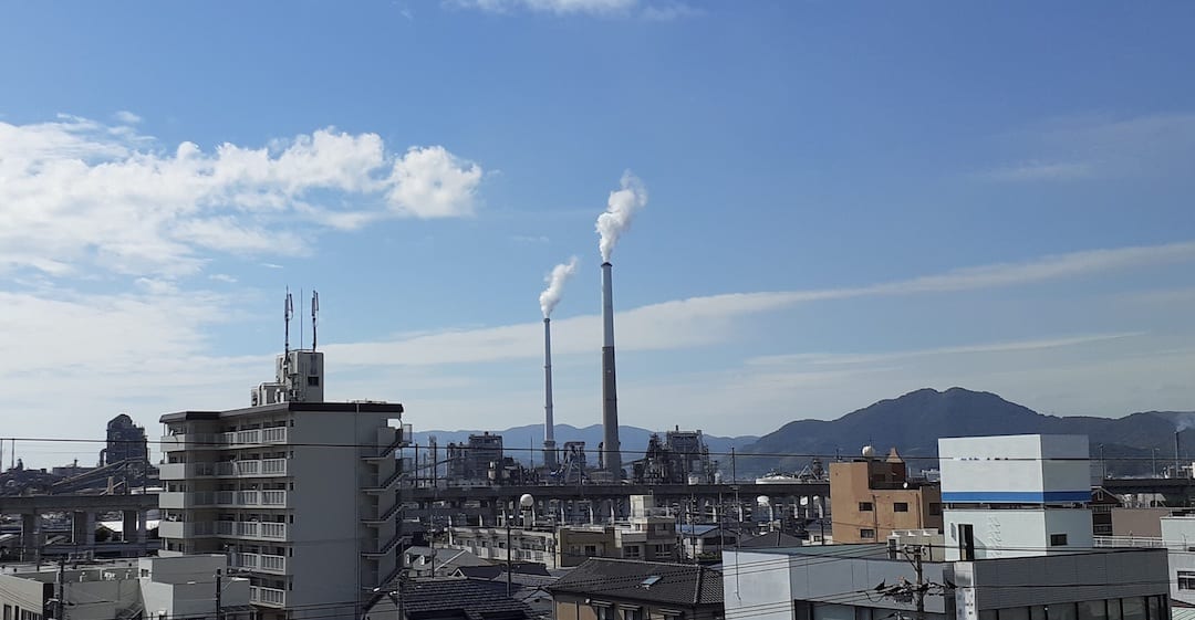 煙突が立ち並ぶ工業地帯と山並みの風景